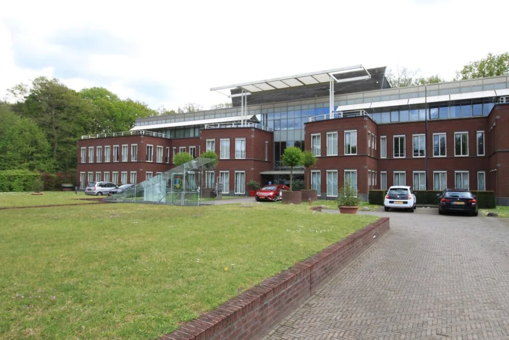 Modern kantoorgebouw aan de Arnhemse Bovenweg met een glazen entree en geparkeerde auto's op de oprijlaan.